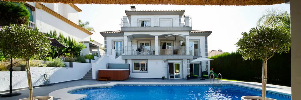 Modern villa with pool, surrounded by greenery and outdoor seating areas.