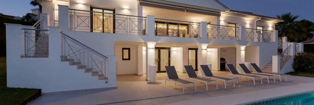 Modern two-storey house with pool, outdoor seating, and stylish design, illuminated at dusk.