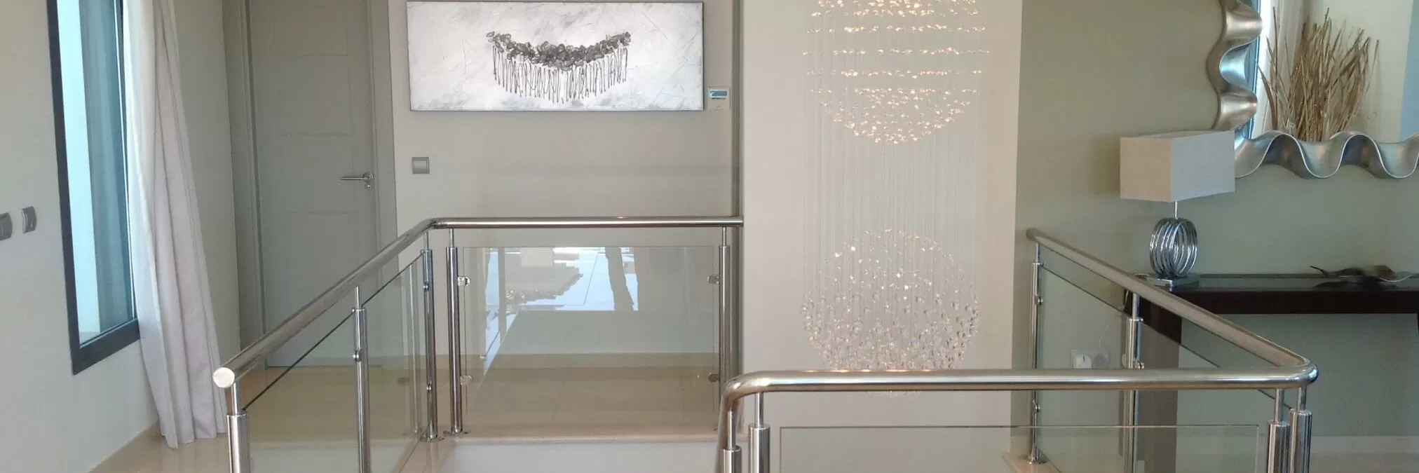 Modern interior with a glass railing, artwork, and decorative lighting fixtures.