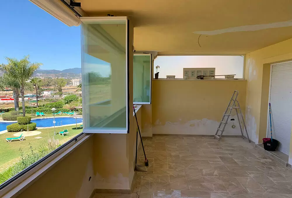 An unfinished room with large windows, a ladder, and a view of a pool area.
