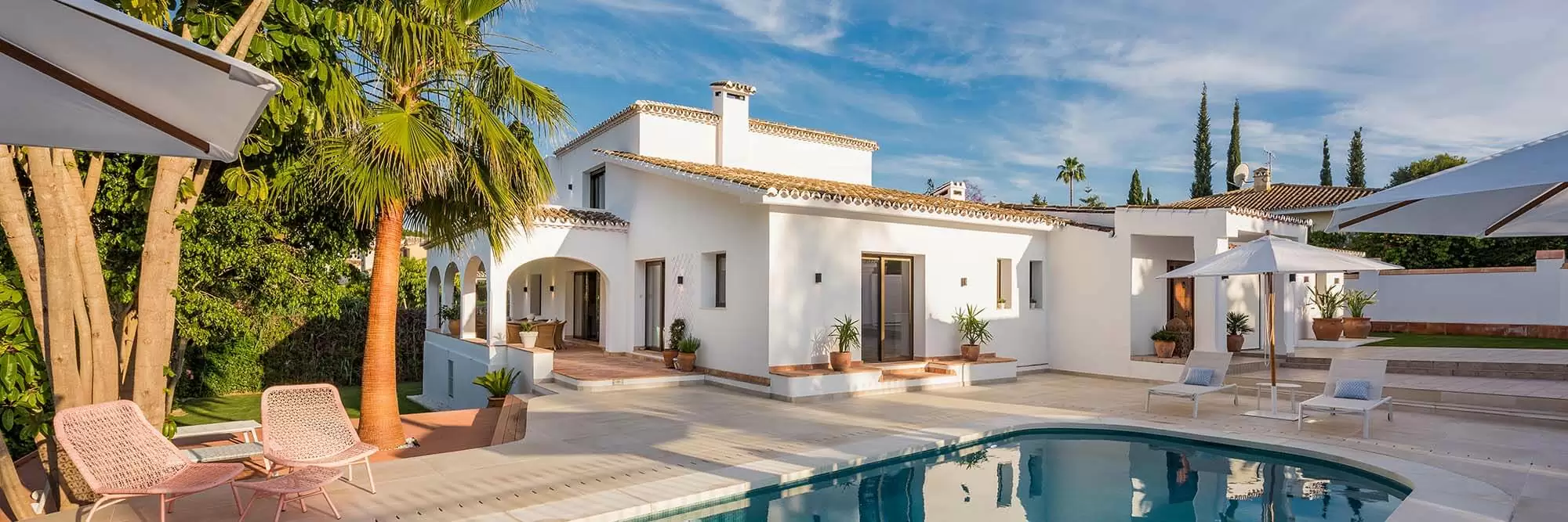 A modern villa features a swimming pool, sun loungers, and lush greenery.